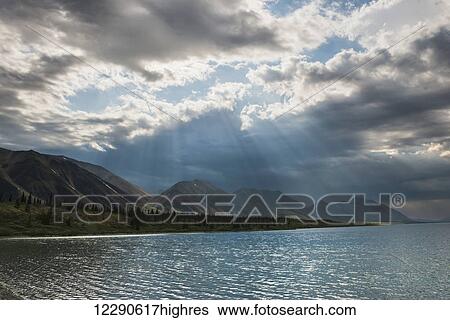 Stock Photograph - Afternoon light shines through a cloud following a storm over lower Twin Lake in Lake Clark National Park & Preserve.. Fotosearch