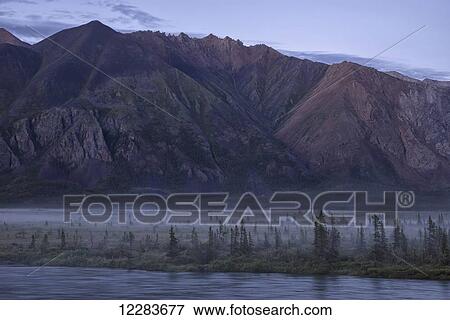 Stock Photo - An evening mist creeps in over the valley and trees along the Wind River in the Peel Watershed; Yukon, Canada. Fotosearch