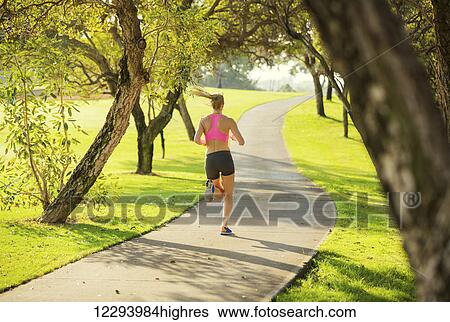 Stock Photograph - Athletic fit young woman jogging running outdoors early morning in park. Healthy lifestyle sports fitness concept.. Fotosearch