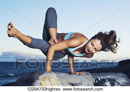 Stock Photograph - Athletic strong woman practicing difficult yoga pose outdoors. Fotosearch