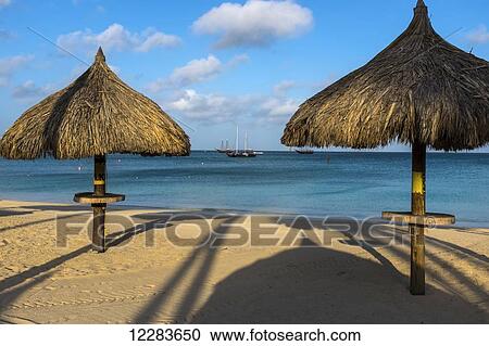 Stock Image - Beach palapas at Palm Beach with sailboats anchored close to shore; Aruba. Fotosearch