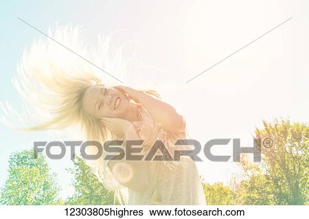 Stock Photograph - Beautiful young woman listening to music and singing along while swinging her long blond hair outdoors in a city park; Edmonton, Alberta, Canada. Fotosearch