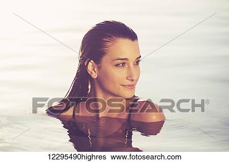 Stock Photograph - Beautiful young woman relaxing in pool at sunset, Luxury resort fashion lifestyle. Fotosearch