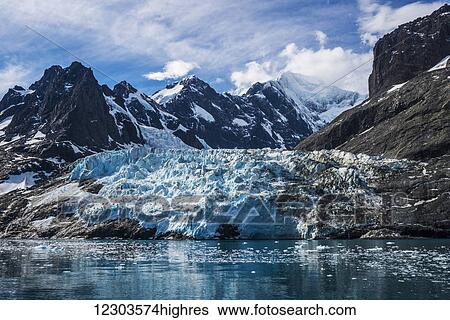 Stock Photograph - Blue glacier between snow-capped mountains and fjord; Antarctica. Fotosearch