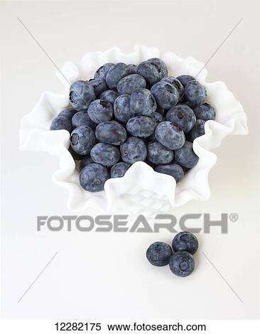 Stock Photography - Blueberries in a white scalloped bowl on a white background; British Columbia, Canada. Fotosearch