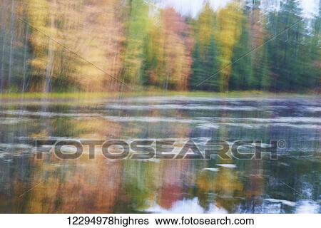 Stock Photograph - Blurred autumn coloured trees along the shoreline reflected in a tranquil river; Ontario, Canada. Fotosearch