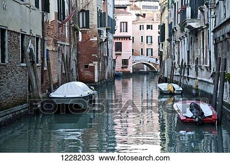 Stock Image - Boats moored along buildings in a tranquil canal; Venice, Italy. Fotosearch