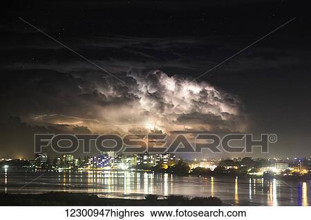 Stock Photograph - Buildings along the coastline illuminated and reflected in the water at nighttime; Brisbane, Queensland, Australia. Fotosearch