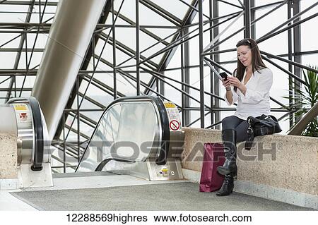 Stock Photograph - Business woman texting on her smart phone after taking a shopping break during her work day; Edmonton, Alberta, Canada. Fotosearch
