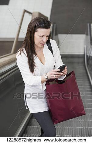 Business woman texting on her smart phone on an escalator after taking a shopping break during her work day; Edmonton, Alberta, Canada View Large Photo Image Stock Photograph - Business woman texting on her smart phone on an escalator after taking a shopping break during her work day; Edmonton, Alberta, Canada. Fotosearch
