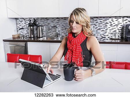 Stock Image - Businesswoman taking a coffee break and checking her tablet; St. Albert, Alberta, Canada. Fotosearch