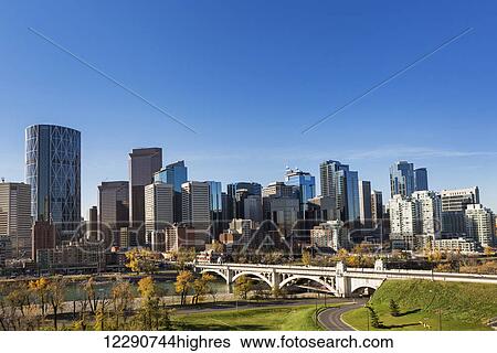 Stock Photograph - Calgary skyline with bridge spanning across river, autumn coloured trees and blue sky; Calgary, Alberta, Canada. Fotosearch