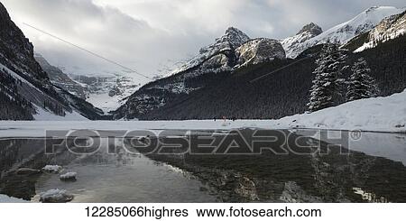 Stock Photograph - Canadian rocky mountains with snow under a cloudy sky reflect in the lake; Lake Louise, Alberta, Canada. Fotosearch