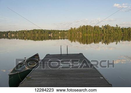 Canoe beside a wooden dock on a tranquil lake; Ontario, Canada View Large Photo Image Stock Image - Canoe beside a wooden dock on a tranquil lake; Ontario, Canada. Fotosearch