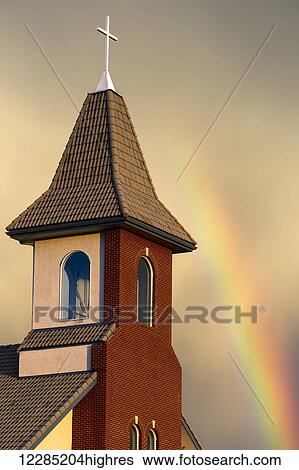 Stock Photograph - Church steeple with orange glow from the sunset and rainbow in the sky; Calgary, Alberta, Canada. Fotosearch