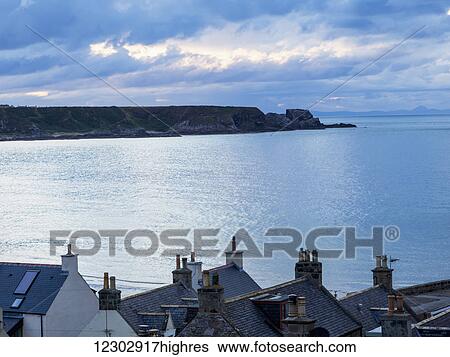 Stock Photograph - Cliffs along the coastline and rooftops of houses in the foreground; Cullen, Moray, Scotland. Fotosearch