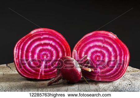 Stock Photograph - Close up of a cut red and white striped beet with an uncut small beet on top of a wooden board and black background; Calgary, Alberta, Canada. Fotosearch