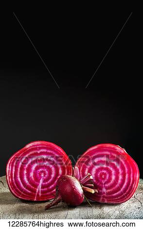 Close up of a cut red and white striped beet with an uncut small beet on top of a wooden board and black background; Calgary, Alberta, Canada View Large Photo Image Stock Photograph - Close up of a cut red and white striped beet with an uncut small beet on top of a wooden board and black background; Calgary, Alberta, Canada. Fotosearch