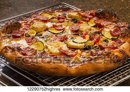Close up of a golden crust oven baked pizza on a cooling rack with roasted zucchini, peppers, artichokes, mushrooms, olives; Calgary, Alberta, Canada View Large Photo Image Stock Photograph - Close up of a golden crust oven baked pizza on a cooling rack with roasted zucchini, peppers, artichokes, mushrooms, olives; Calgary, Alberta, Canada. Fotosearch