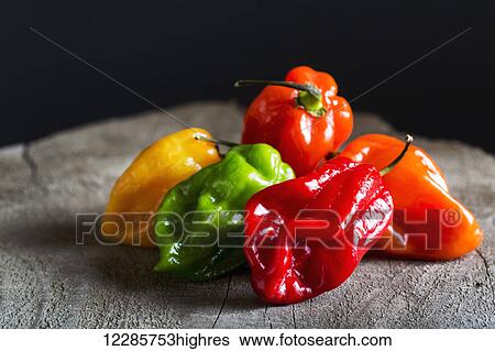 Stock Photograph - Close up of assorted colourful hot peppers on wooden board and black background; Calgary, Alberta, Canada. Fotosearch