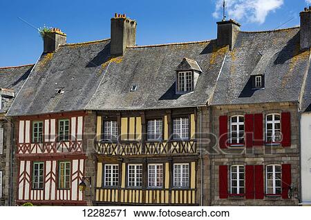 Stock Image - Close up of colourfully painted half timbered stone buildings and shutters with blue sky and clouds; Treguier, Brittany, France. Fotosearch