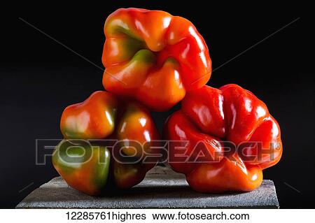 Close up of the bottoms of three colourful and interesting shaped red/green peppers on top of each other on a wooden board and black background; Calgary, Alberta, Canada View Large Photo Image Stock Photograph - Close up of the bottoms of three colourful and interesting shaped red/green peppers on top of each other on a wooden board and black background; Calgary, Alberta, Canada. Fotosearch