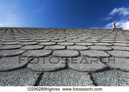 Stock Photograph - Close up of well worn rounded roof shingles with intersting contours and blue sky; Calgary, Alberta, Canada. Fotosearch