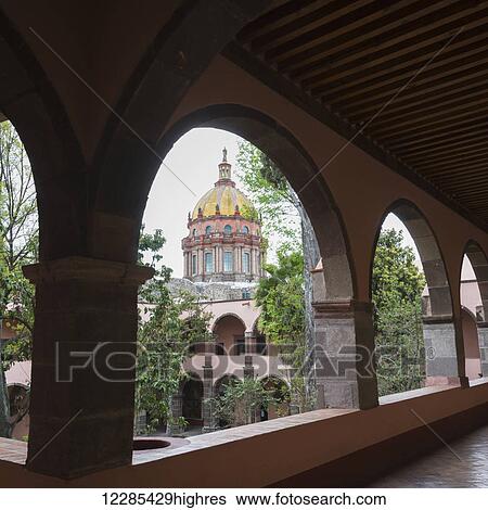 Stock Photograph - Colourful Church of the Nuns with dome viewed through arches; San Miguel de Allende, Guanajuato, Mexico. Fotosearch
