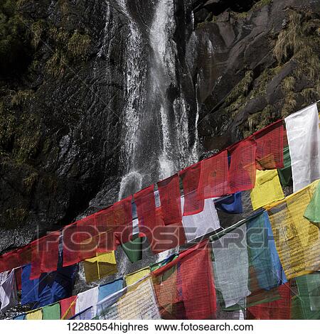 Stock Photograph - Colourful prayer flags and a waterfall down a cliff in the background; Paro, Bhutan. Fotosearch