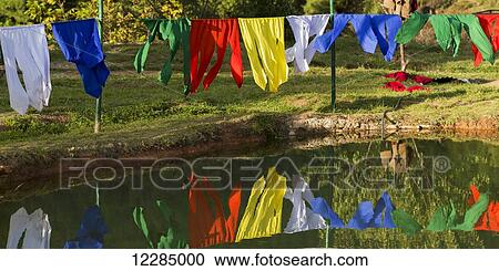 Stock Image - Colourful prayer flags hanging and reflected in the water; Paro, Bhutan. Fotosearch