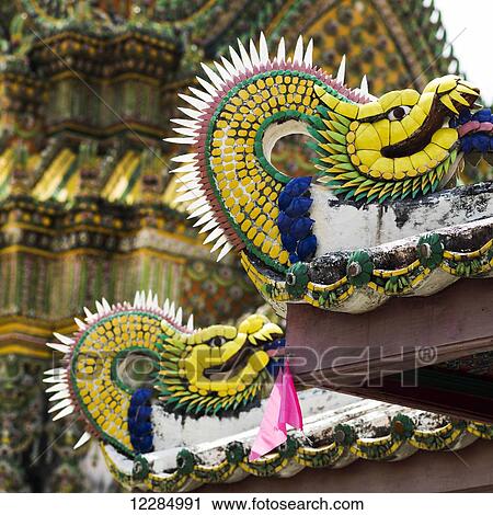 Stock Image - Colourful sculpture of a dragon with an ornate building in the background; Bangkok, Thailand. Fotosearch