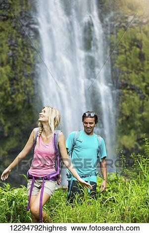 Stock Photograph - Couple having fun together outdoors on hike to amazing waterfall in Hawaii.. Fotosearch