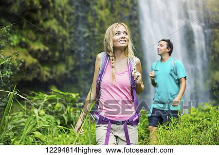 Stock Photograph - Couple having fun together outdoors on hike to amazing waterfall in Hawaii.. Fotosearch