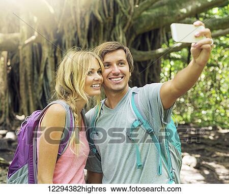 Stock Photograph - Couple having fun together outdoors. Taking self portrait with camera phone on hike.. Fotosearch