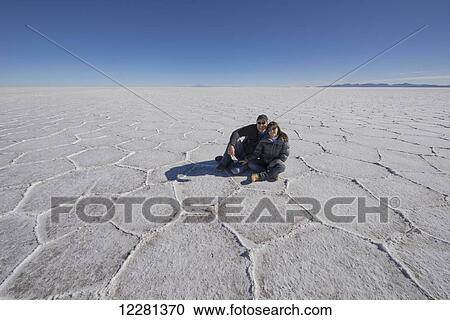 Stock Image - Couple sitting on the salt flats of the Salar de Uyuni; Bolivia. Fotosearch