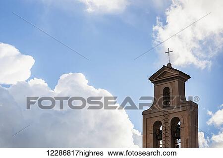 Stock Photograph - Cross and bell tower of a church against a blue sky with cloud; Rome, Italy. Fotosearch