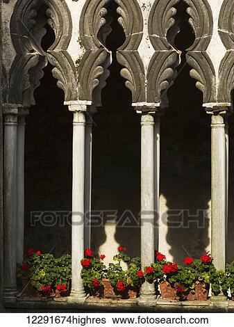 Stock Photograph - Decorative pillars and a facade of a building with red flowers lining a ledge; Amalfi, Campania, Italy. Fotosearch