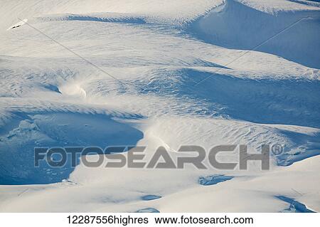 Stock Photograph - Deep blue shadows cast on a varied snowy landscape above Kings Bay, Prince William Sound; Whittier, Alaska, United States of America. Fotosearch