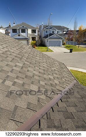Stock Photograph - Detail of brand new roof shingles with neighbourhood houses, autumn colours and blue sky in the background; Calgary, Alberta, Canada. Fotosearch
