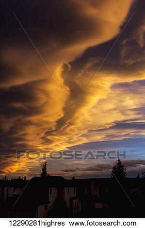 Stock Photograph - Dramatic colourful clouds at sunset with interesting formations and some blue sky with houses in a neighbourhood; Calgary, Alberta, Canada. Fotosearch