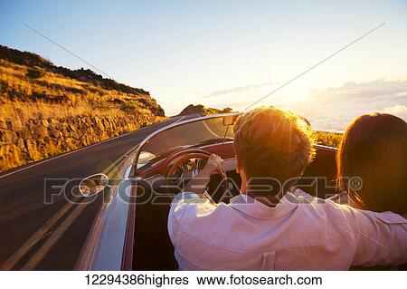 Stock Photograph - Driving into the Sunset. Romantic Young Couple Enjoying Sunset Drive in Classic Vintage Sports Car. Fotosearch