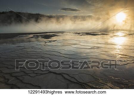 Stock Photograph - Evening light shines through the steam rising over the Grand Prismatic Spring in Yellowstone National Park; Wyoming, United States of America. Fotosearch