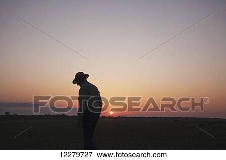 Stock Photo - Farmer checking his field of seedling corn as sun rises; England, Arkansas, United States of America. Fotosearch