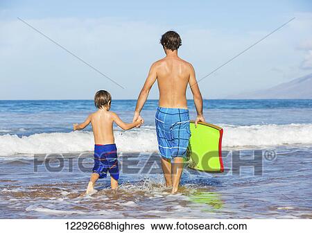 Stock Photograph - Father and Son Going Surfing Together on Tropical Beach in Hawaii. Fotosearch