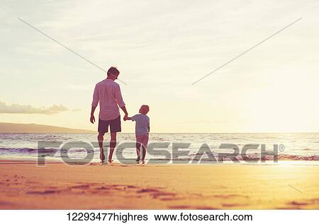 Stock Photograph - Father and Son Holding Hands Walking Together on the Beach at Sunset. Fotosearch