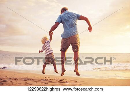 Stock Photograph - Father and son jumping for joy on the beach at sunset. Fotosearch