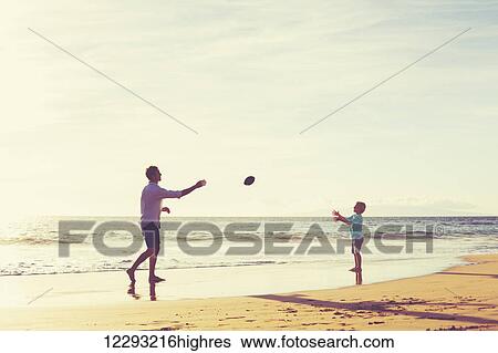 Stock Photograph - Father and Son Playing Catch Throwing Football on the Beach at Sunset. Fotosearch