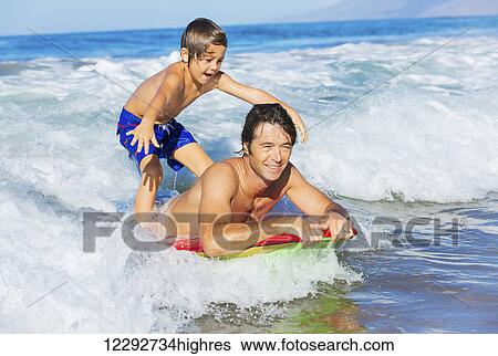 Stock Photograph - Father and Son Surfing Tandem Together Catching Ocean Wave, Carefree happy fun smiling lifestyle. Fotosearch