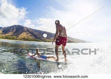 Stock Photograph - Father and Son Surfing Together. Riding Wave on Surfboard Tandem. Fatherhood, Family Fun Outdoor Lifestyle.. Fotosearch