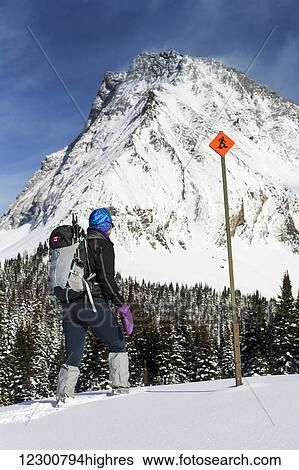 Female snowshoer on snow covered hillside with snow covered mountains and trees in the background with snowshoe sign and blue sky with clouds; Kananaskis Country, Alberta, Canada View Large Photo Image Stock Photograph - Female snowshoer on snow covered hillside with snow covered mountains and trees in the background with snowshoe sign and blue sky with clouds; Kananaskis Country, Alberta, Canada. Fotosearch